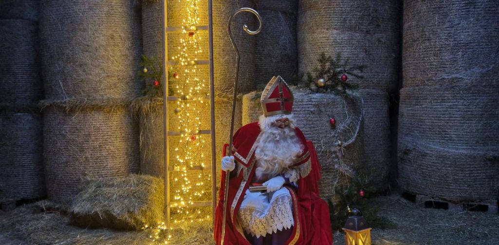 Der Nikolaus sitzend vor Heuballen im Stall von Eva. Eine Lichterkette erstreckt sich von der Leiter bis vor dem Mann zu einer Laterne