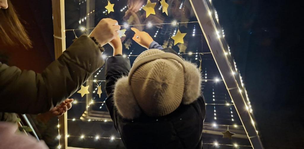 Verena Eder Ein Kind hängt mit Hilfe eines Erwachsenen einen Stern auf den Baum