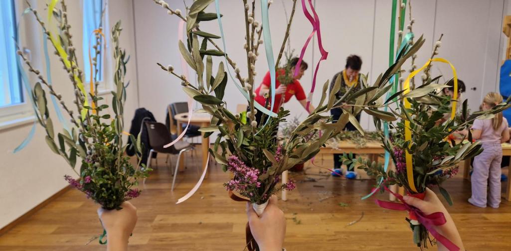 Die Kinder heben ihre Palmbuschen in die Höhe und im Hintergrund sind die Pollinger Bäuerinnen zu sehen