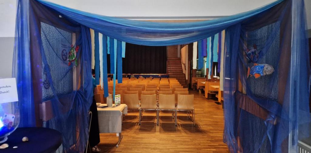Der Eingangsbereich des Vereinshauses, blauer Tüll ist von einer Schwingtüre zur anderen gespannt, durch diesen Wellenbogen gelangt man in die Halle