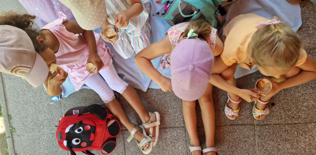 Vier Kinder von oben fotografiert. Sie sitzen auf einer Decke und halten einen Eisbecher in der HAnd