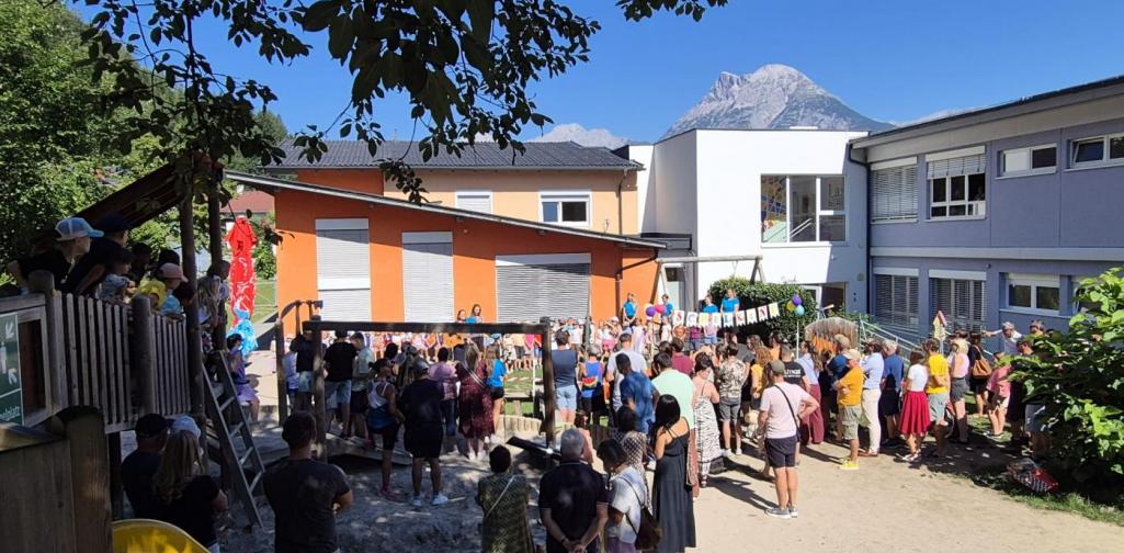 Der Garten des Kindergartens beim Fest von der Rutsche aus fotografiert. Alle Gäste stehen vor den Schulkindern